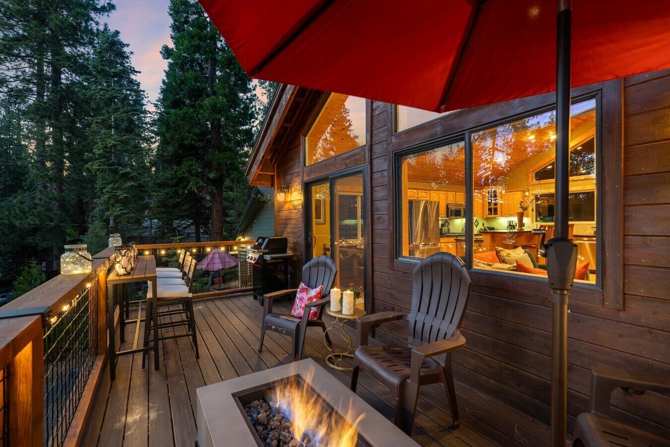 A wooden deck with outdoor seating, a fire pit, and a view of the interior kitchen.