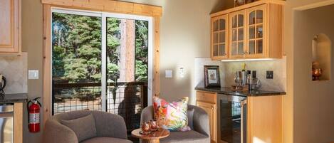 A cozy cabin interior with a dining area, a kitchen, and a large window offering a forest view.