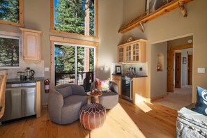 Un vaste espace de vie comprenant une cuisine, un coin repas et une grande fenêtre donnant sur une forêt.