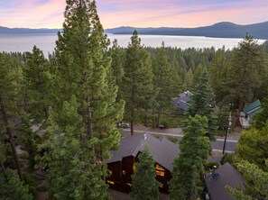 Une cabane entourée d’une forêt dense, avec vue sur un lac et des montagnes au loin.