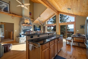 A spacious kitchen with a stone fireplace, wooden ceiling, and large windows offering a view of the outdoors. - Brand New Kings Beach Retreat  Lake Views + Forest (Kings Beach)