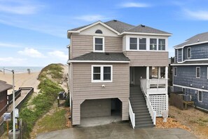 A two-story house with a garage, a covered porch, and a view of the beach. - 5754 - An Unforgettable Vacation - Luxury Oceanfront | Private Pool & Game Room (Nags Head)