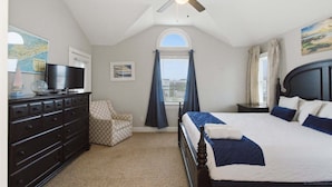 Ein Schlafzimmer mit einem Bett, einem Schminktisch, einem Sessel, einem Deckenventilator und einem Fenster mit Vorhängen.