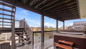 Eine Holzterrasse mit Whirlpool und Bänken mit Blick auf Strand und Häuser.