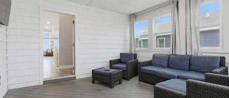 A covered outdoor seating area with wicker furniture and a view of the adjacent building.