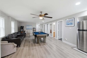 A modern living room with a pool table, a ceiling fan, and a refrigerator. - 5754 - An Unforgettable Vacation - Luxury Oceanfront | Private Pool & Game Room (Nags Head)