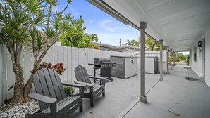 A covered patio with two Adirondack chairs, a grill, and a white fence. - 600 #2 Managed by Brampton Park (Deerfield Beach)