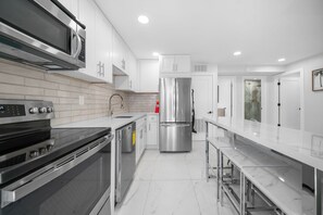 A modern kitchen with stainless steel appliances, white cabinetry, and a marble countertop. - 600 #2 Managed by Brampton Park (Deerfield Beach)
