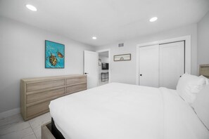 Quarto com uma cama, cômoda de madeira, pintura e porta para um banheiro.