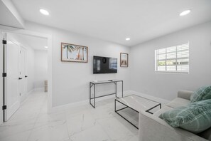 Un salon moderne avec un téléviseur à écran plat, une table basse en verre, un canapé et deux tableaux encadrés accrochés au mur.