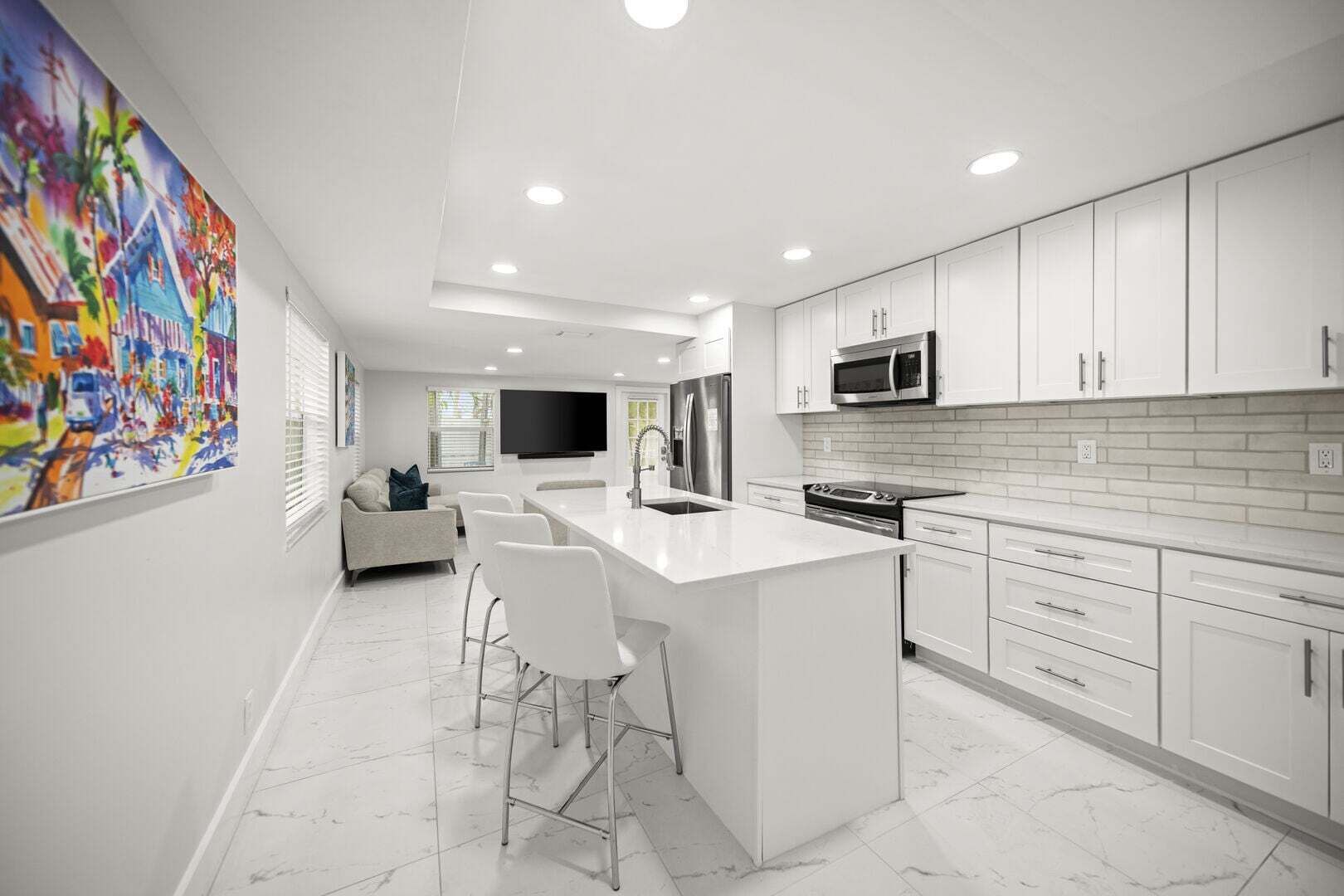 Une cuisine moderne avec des meubles blancs, un îlot central, des appareils en acier inoxydable et un grand tableau accroché au mur.