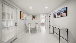 Um corredor com área de refeições, paredes brancas e piso de mármore.