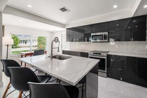 A modern kitchen with a central island, black cabinets, stainless steel appliances, and a large window providing a view of the outdoors. - 237 Managed by Brampton Park (Delray Beach)