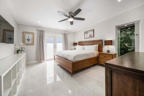 Ein modernes Schlafzimmer mit einem hölzernen Bett, einem Deckenventilator, einer Glasdusche und einer weißen Ablagefläche.