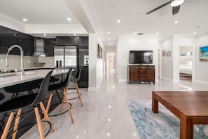A modern kitchen with a dining area, a TV, and a wooden dining table. - 237 Managed by Brampton Park (Delray Beach)