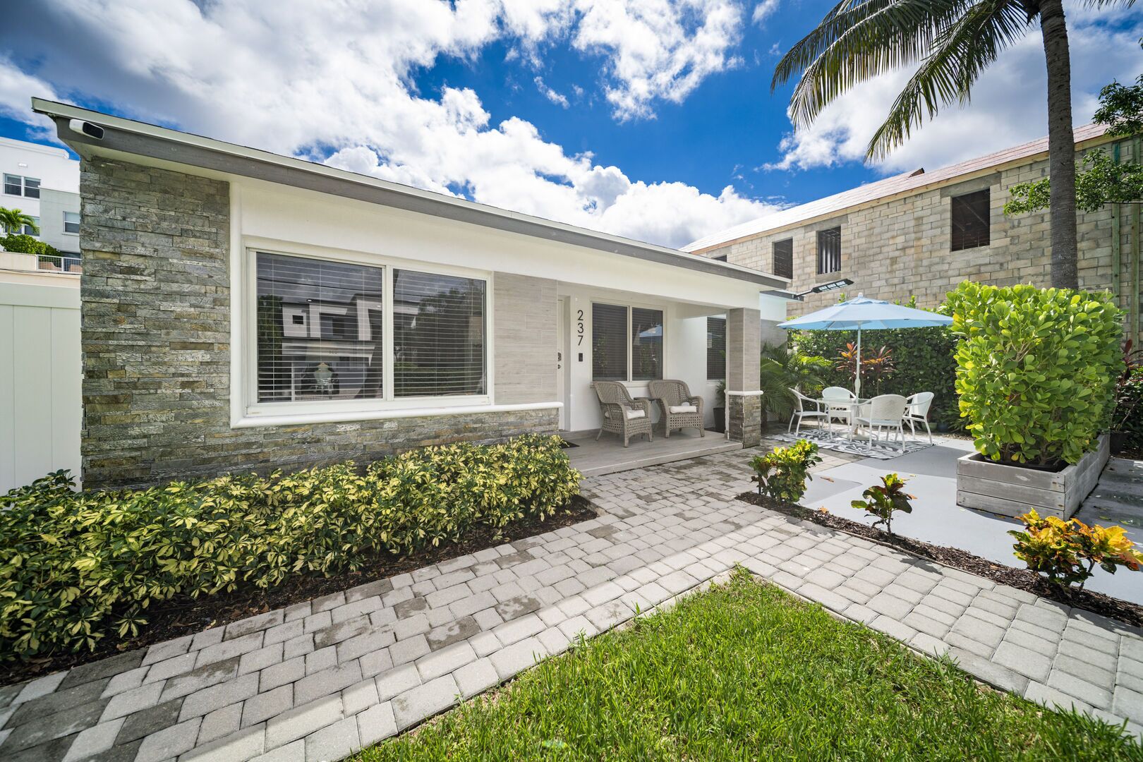 Une maison moderne avec une façade en pierre, un patio doté de mobilier d’extérieur et un jardin bien entretenu.