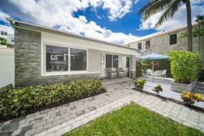 A modern house with a stone facade, a patio with outdoor furniture, and a well-maintained garden. - 237 Managed by Brampton Park (Delray Beach)
