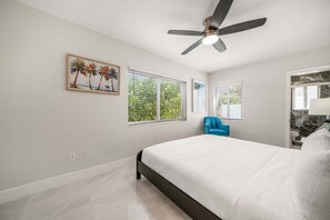 Een slaapkamer met een bed, een plafondventilator, een raam met zonwering en een schilderij aan de muur.