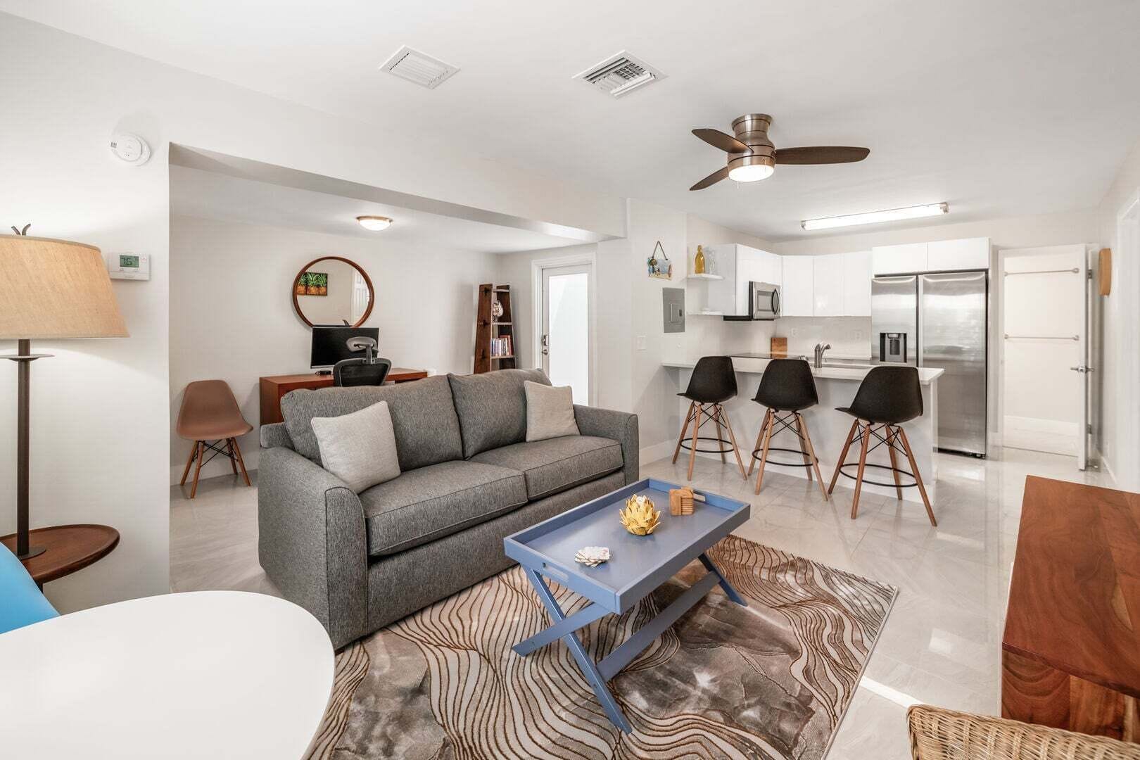 A modern living room with a gray sofa, a coffee table, and a dining area with black chairs.