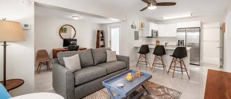 A modern living room with a gray sofa, a coffee table, and a dining area with black chairs.