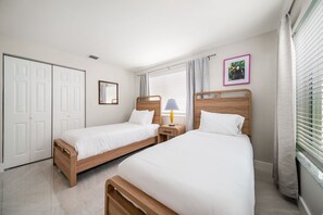 A hotel room with two single beds, a wooden headboard, a bedside table with a lamp, a wardrobe, and a window with blinds. - 237B Managed by Brampton Park (Delray Beach)