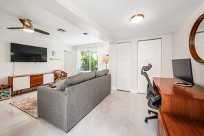 Uma sala de estar moderna com sofá, TV, escrivaninha e ventilador de teto.