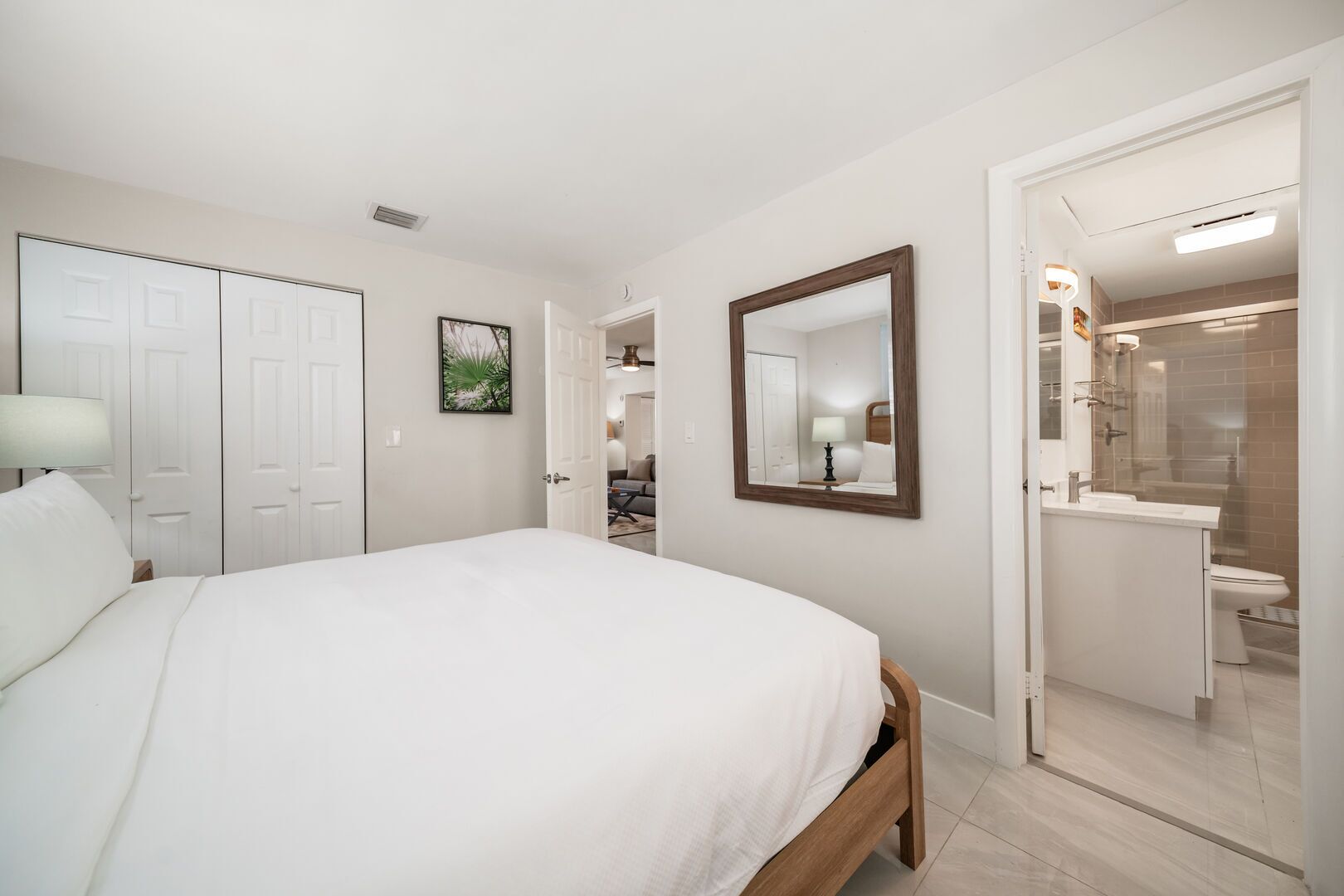 A hotel room with a bed, a bathroom with a shower, and a door leading to another room.