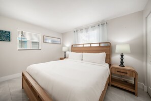 A bedroom with a wooden bed, two bedside tables with lamps, a window with blinds, and a wall-mounted picture. - 237B Managed by Brampton Park (Delray Beach)