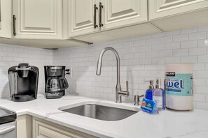 A kitchen with white cabinets, a stainless steel sink, a coffee maker, a toaster, and a roll of paper towels. - 2240 Managed by Brampton Park (Pompano Beach)