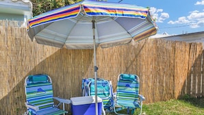A backyard with a striped umbrella, two striped lounge chairs, and a cooler. - 2240 Managed by Brampton Park (Pompano Beach)