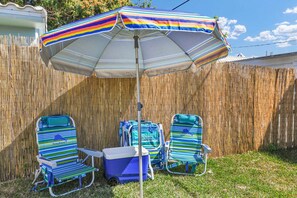 Ein Garten mit einem gestreiften Sonnenschirm, zwei gestreiften Liegestühlen und einer Kühlbox.