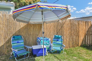 Um quintal com um guarda-sol listrado, duas cadeiras de praia e um cooler.