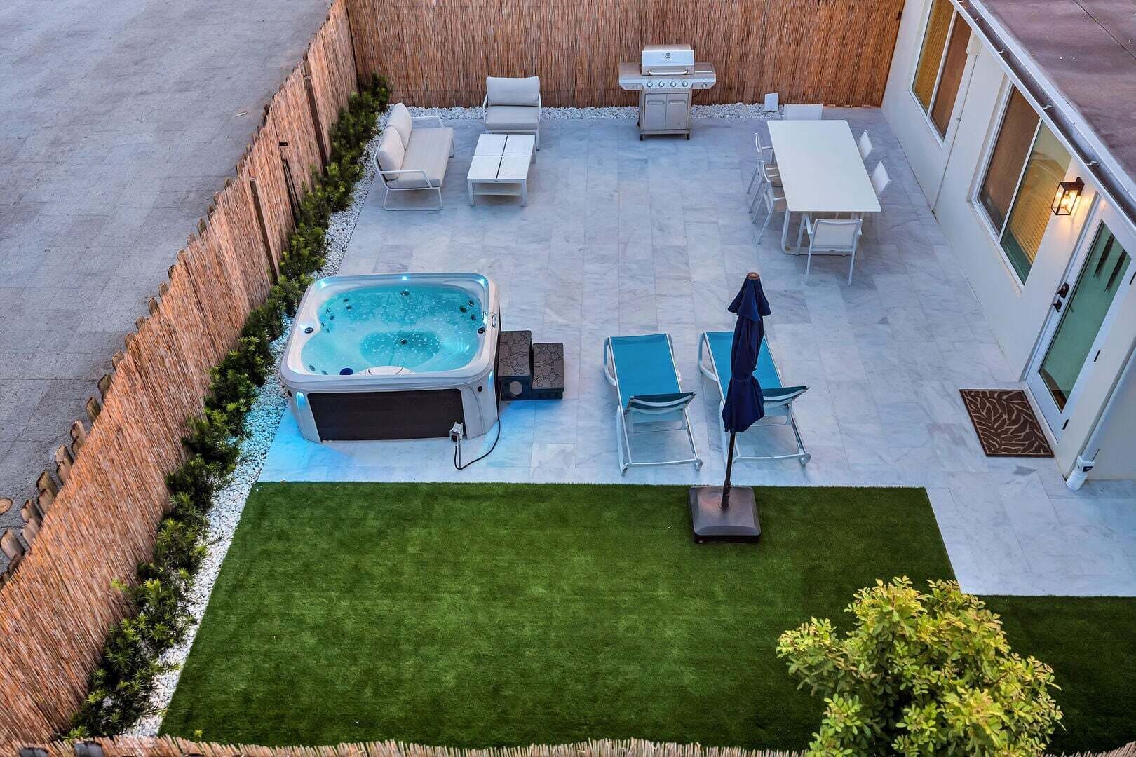 Ein Terrassenbereich mit Whirlpool, Liegestühlen, einem Tisch und einem Grill.