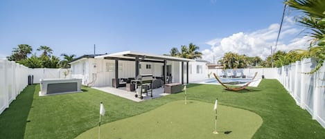 Un patio trasero con césped artificial, una piscina y un porche cubierto.