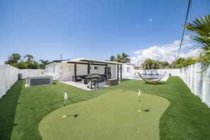 Ein Garten mit Kunstgrasanlage, einem Pool und einer überdachten Terrasse.