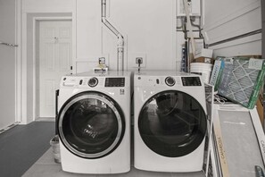 Zwei Waschmaschinen mit Frontlader in einem Waschraum, mit einer weißen Tür und einem Durchlauferhitzer an der Wand.