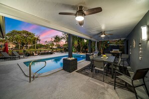 A poolside area with a pool, lounge chairs, a dining table, and ceiling fans. - 1750 Managed by Brampton Park (Pompano Beach)