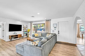 A modern living room with a sectional sofa, a flat-screen TV, a wooden coffee table, and a brick-patterned wall. - 1750 Managed by Brampton Park (Pompano Beach)