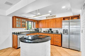 A modern kitchen with wooden cabinets, a stainless steel refrigerator, and a central island. - 1750 Managed by Brampton Park (Pompano Beach)