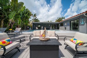 A poolside area with lounge chairs, a small sailboat decoration, and a building with an anchor sign. - 1750 Managed by Brampton Park (Pompano Beach)