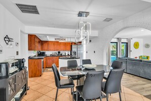 A modern kitchen with wooden cabinets, a dining area with a glass table and chairs, and a view of a pool through the window. - 1750 Managed by Brampton Park (Pompano Beach)