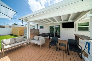 Un patio abrité avec un canapé, des fauteuils, une table et un téléviseur.