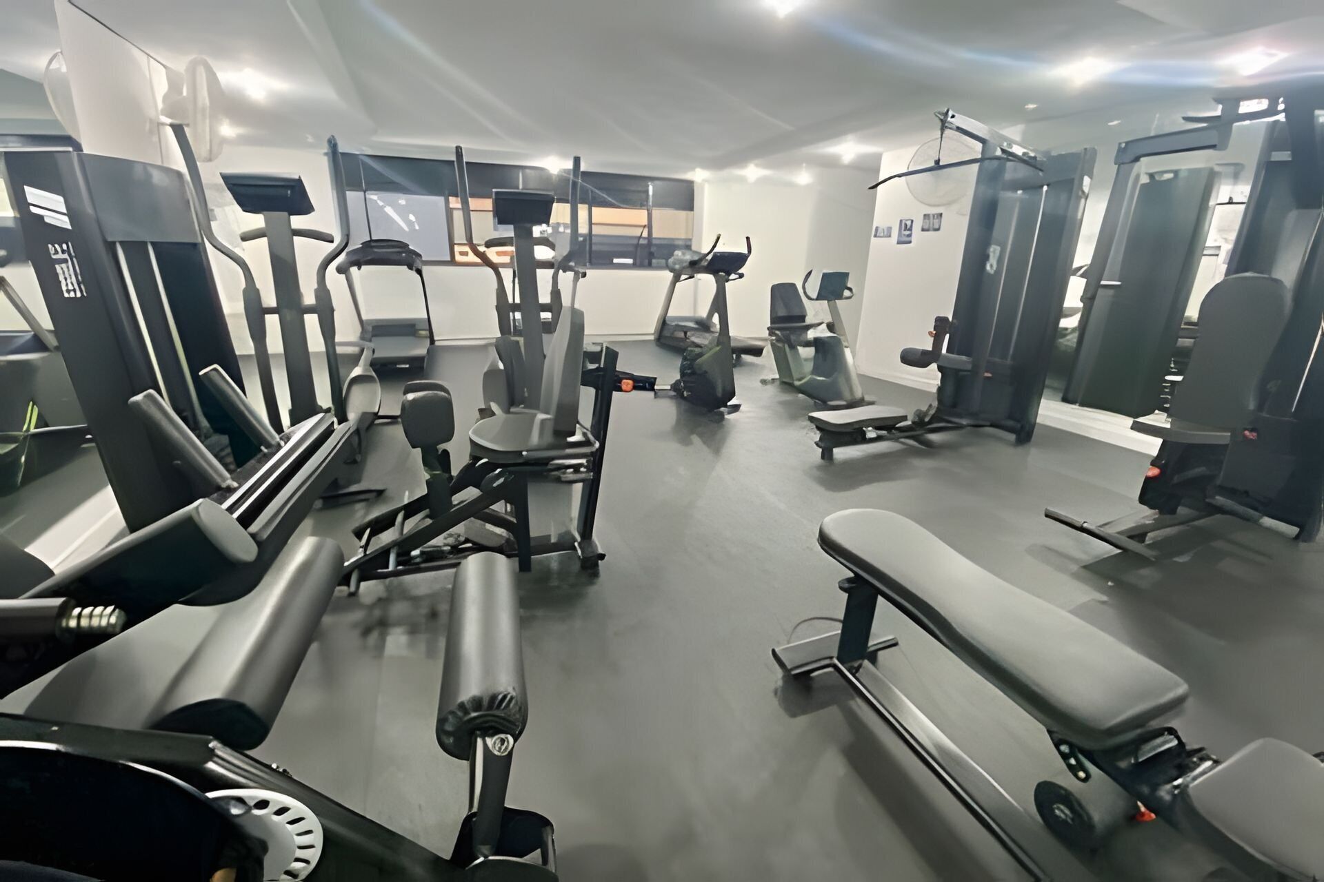 Un gimnasio con diverso equipamiento de ejercicio, incluyendo cintas de correr, máquinas de pesas y bancos.