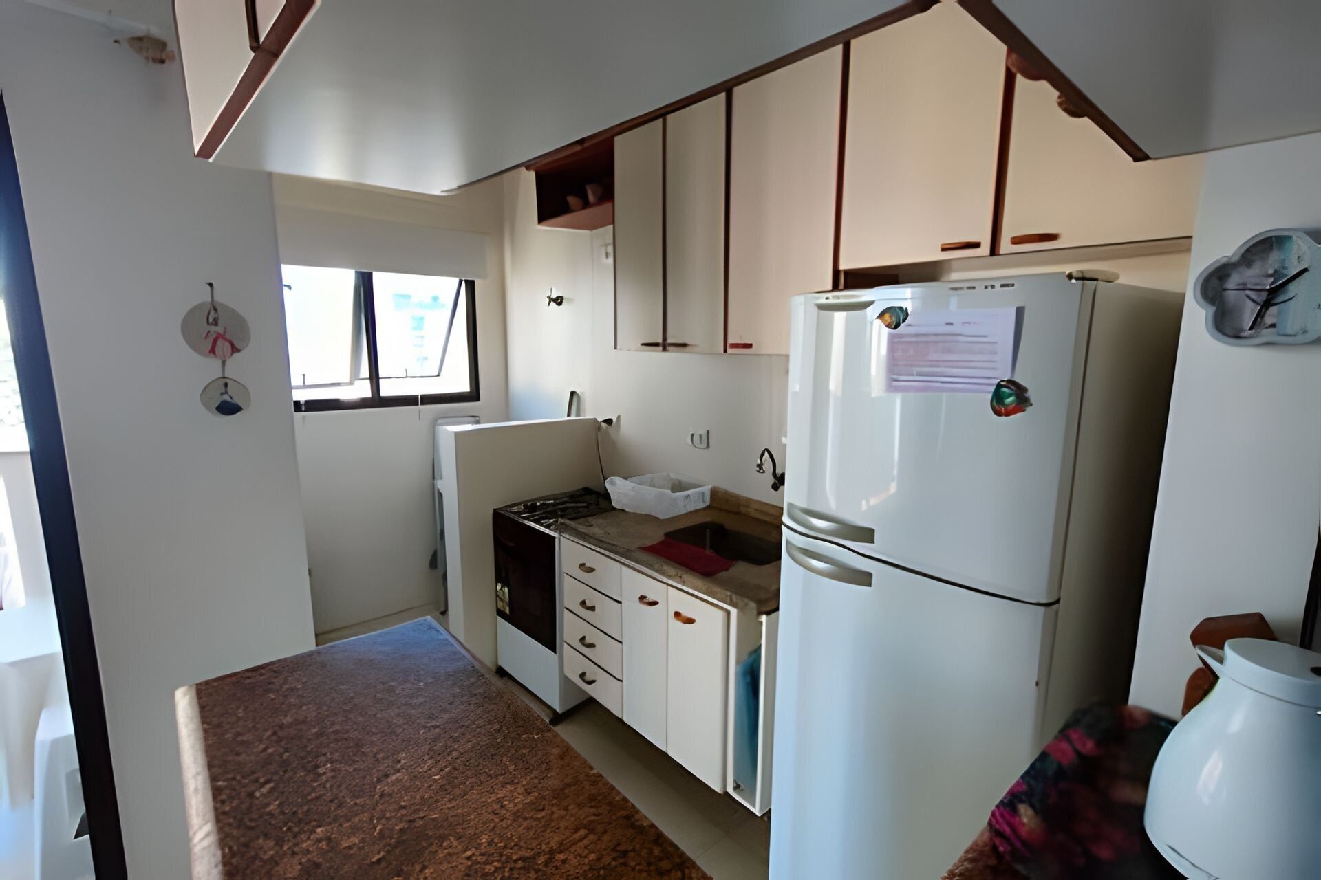 Una cocina compacta con armarios blancos, estufa integrada, lavamanos y refrigerador.