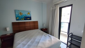 Habitación de hotel con cama, un cuadro, una mesita de noche, una lámpara, una ventana con cortinas y un balcón.