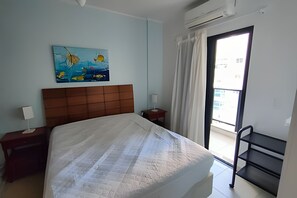 Habitación de hotel con cama, un cuadro, una mesita de noche, una lámpara, una ventana con cortinas y un balcón.