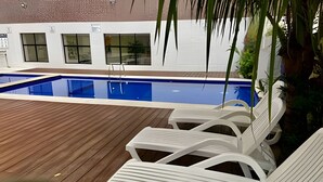 A swimming pool with white lounge chairs and a wooden deck. - SHB Lazer completo no melhor do Guarujá (Guarujá)