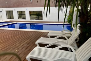 A swimming pool with white lounge chairs and a wooden deck. - SHB Lazer completo no melhor do Guarujá (Guarujá)