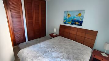 A bedroom with a bed, a nightstand, a wall-mounted painting, and a wooden wardrobe.