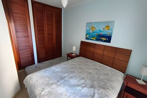 Une chambre à coucher comprenant un lit, une table de chevet, un tableau accroché au mur et une armoire en bois.